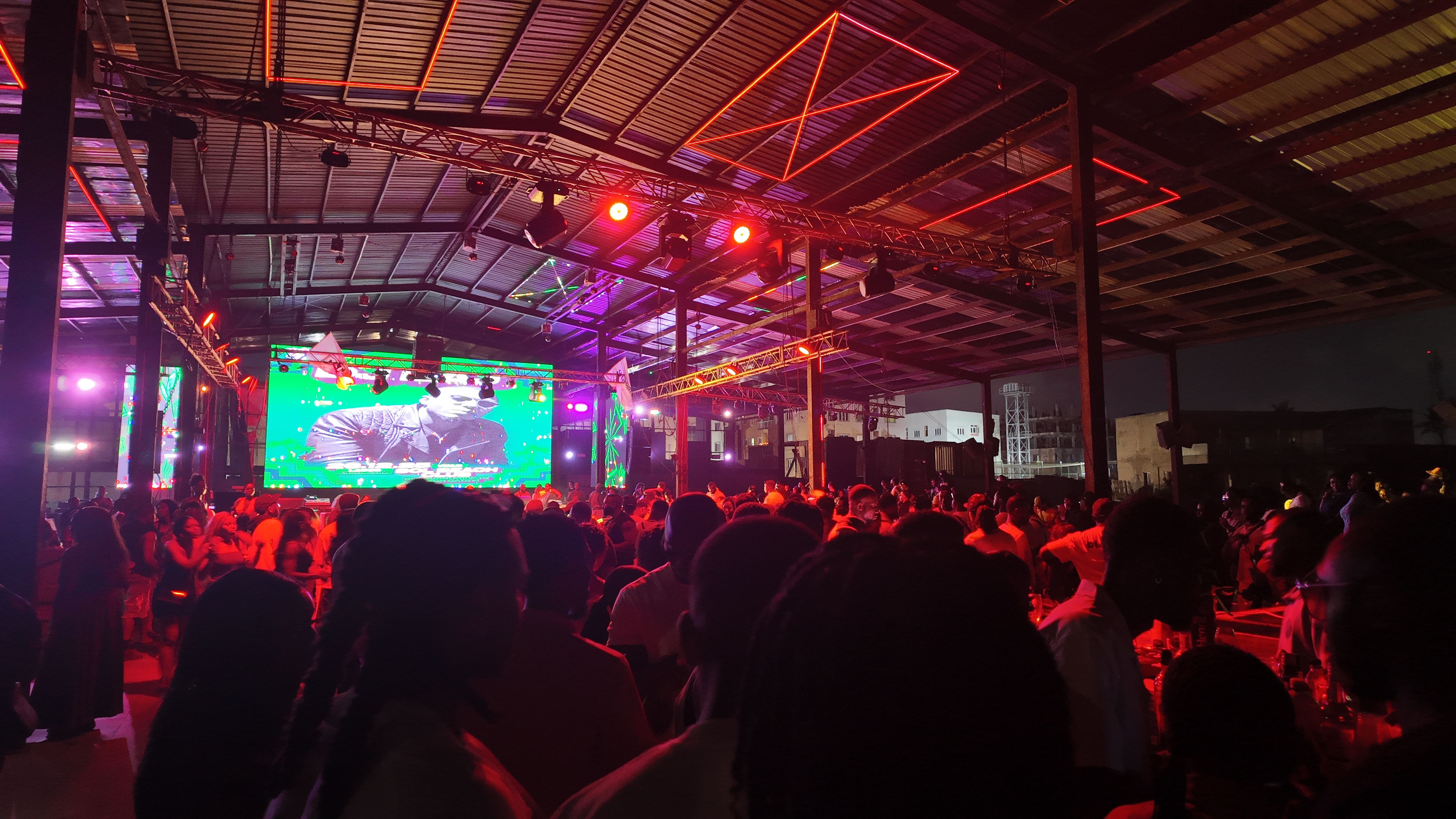 IJGB Connect nightlife — packed crowd under red and purple lights with a green LED screen on stage