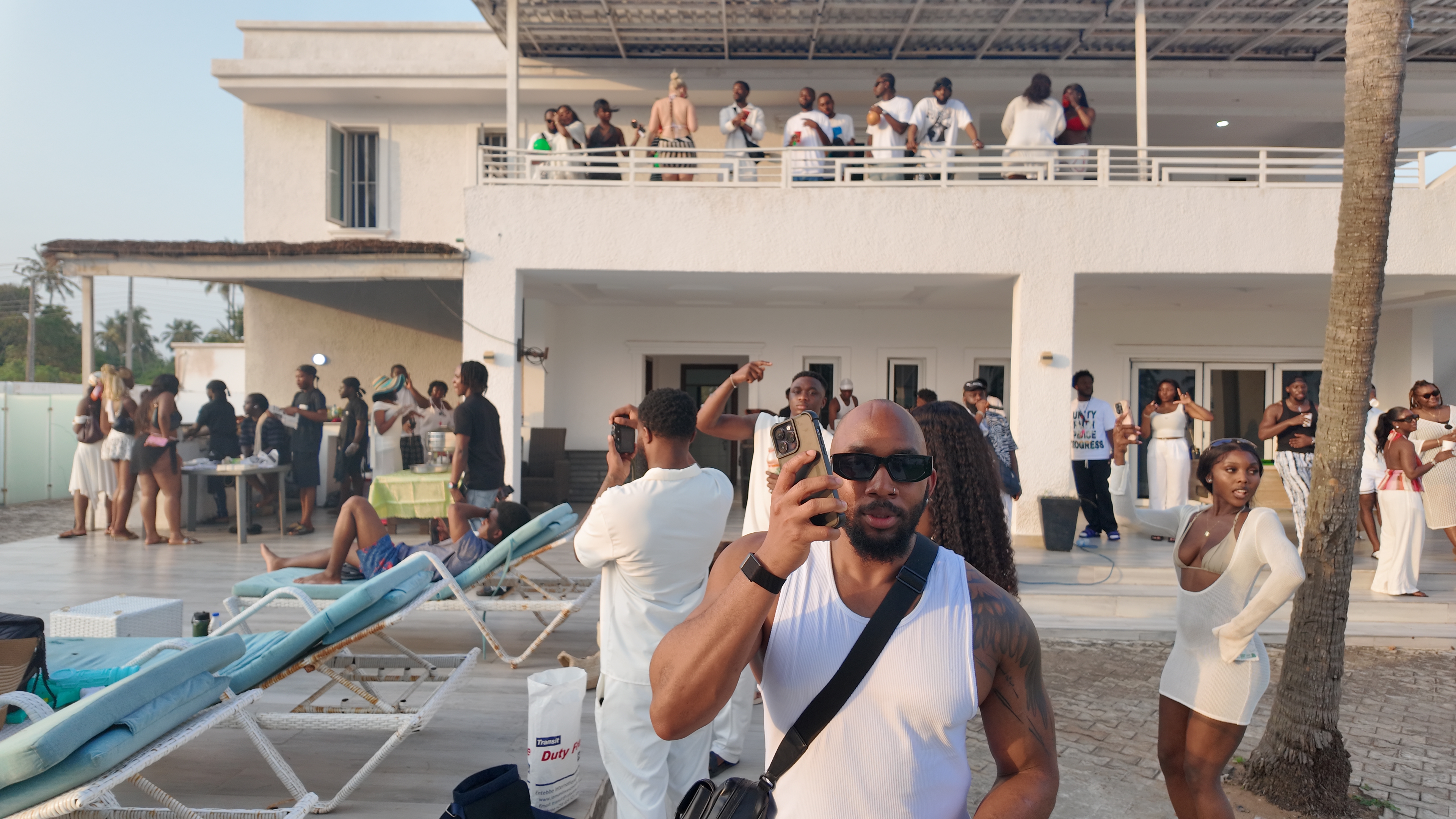 IJGB Connect white party — guest on the phone by the pool with the crowd behind him